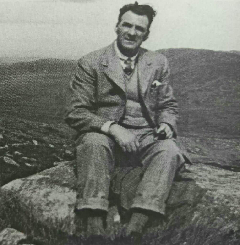 The black and white photograph shows Arthur Kingsley Porter sitting on a rock.